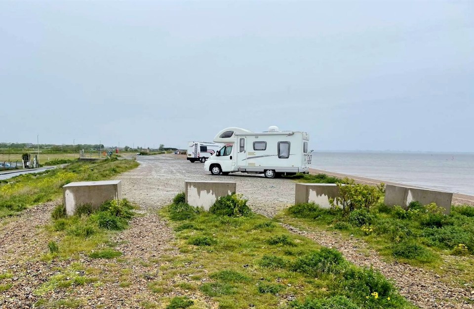 a white rv is parked on a gravel road near the ocean