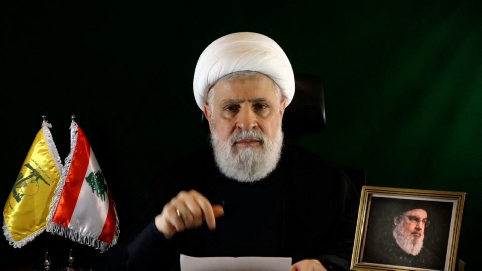 Qassem speaking on October 15 with a photo of Nasrallah next to him