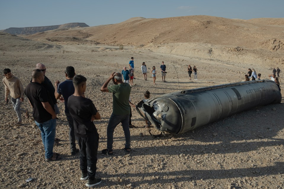 People stand near the remains of a missile in Israel following strikes