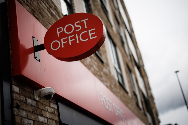 a red post office sign hangs from the side of a building