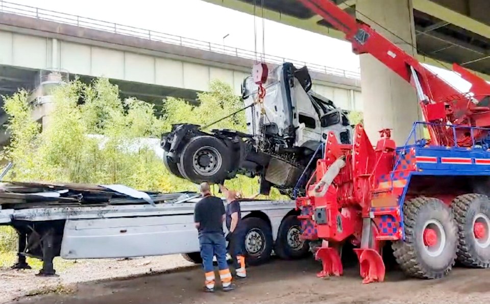 a truck is being lifted by a crane under a bridge