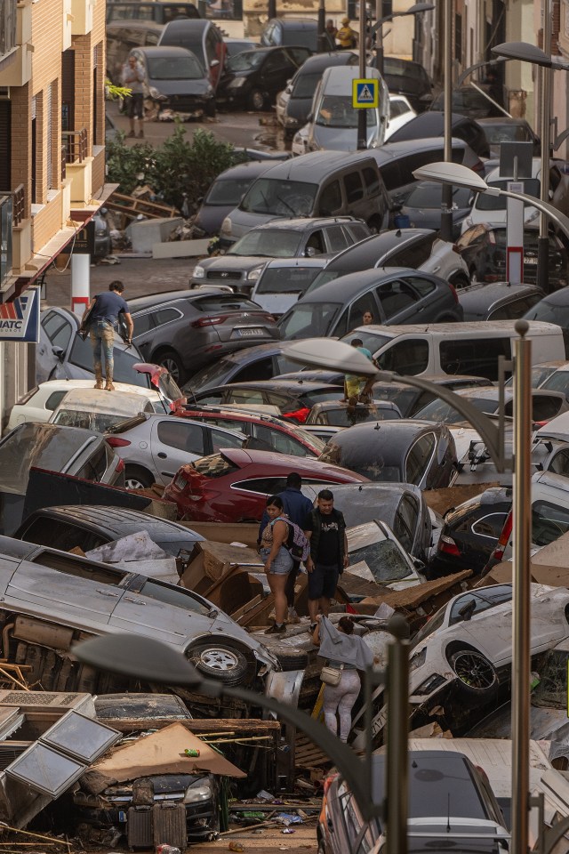 People climb over piles of cars washed into a street