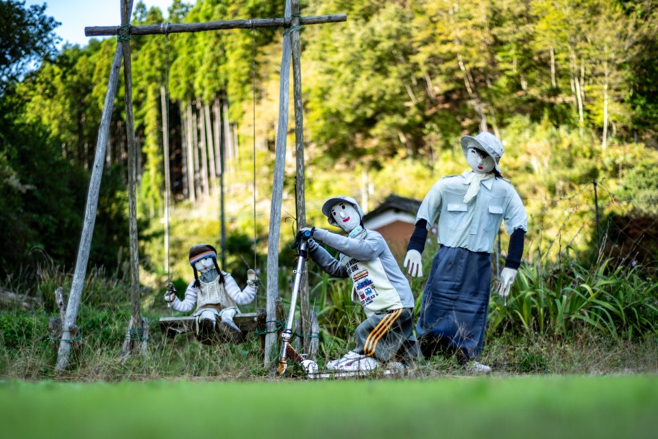 A child doll uses the swing as her brother rides a scooter with the mannequin mum watching on