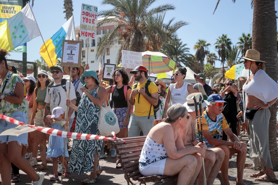 a crowd of people holding signs including one that says time to squat your holiday home