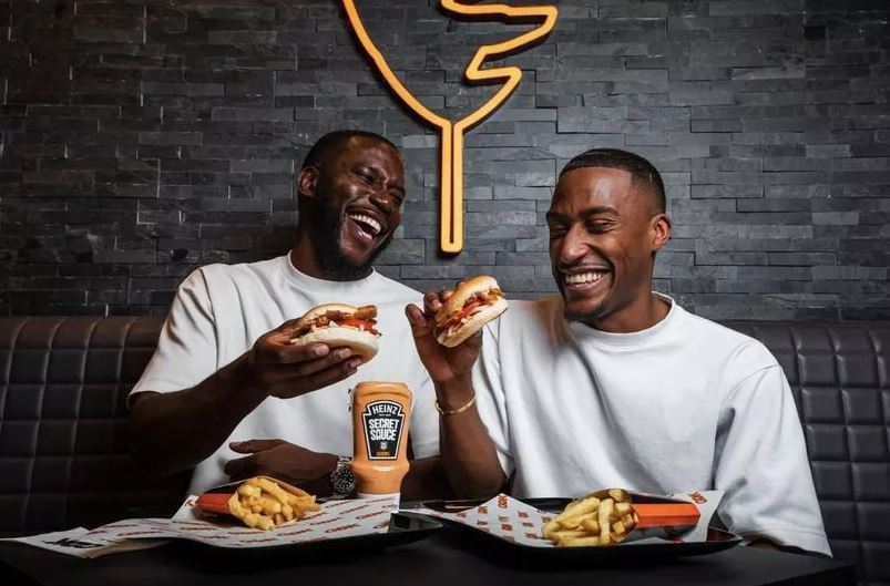 two men are sitting at a table eating hamburgers and french fries .