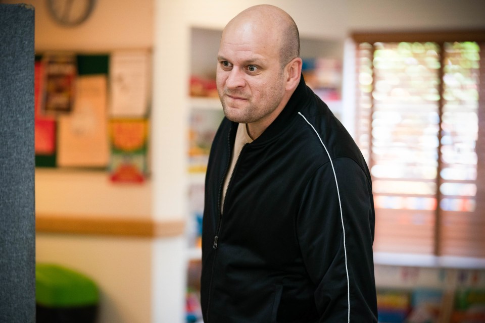 a bald man in a black jacket stands in a room