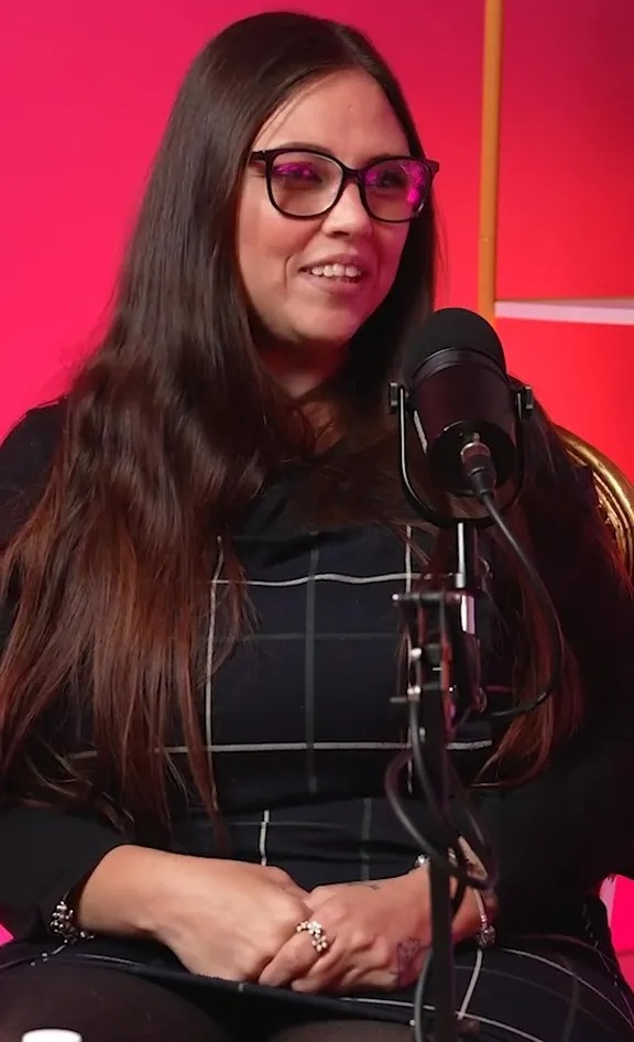 a woman wearing glasses sits in front of a microphone