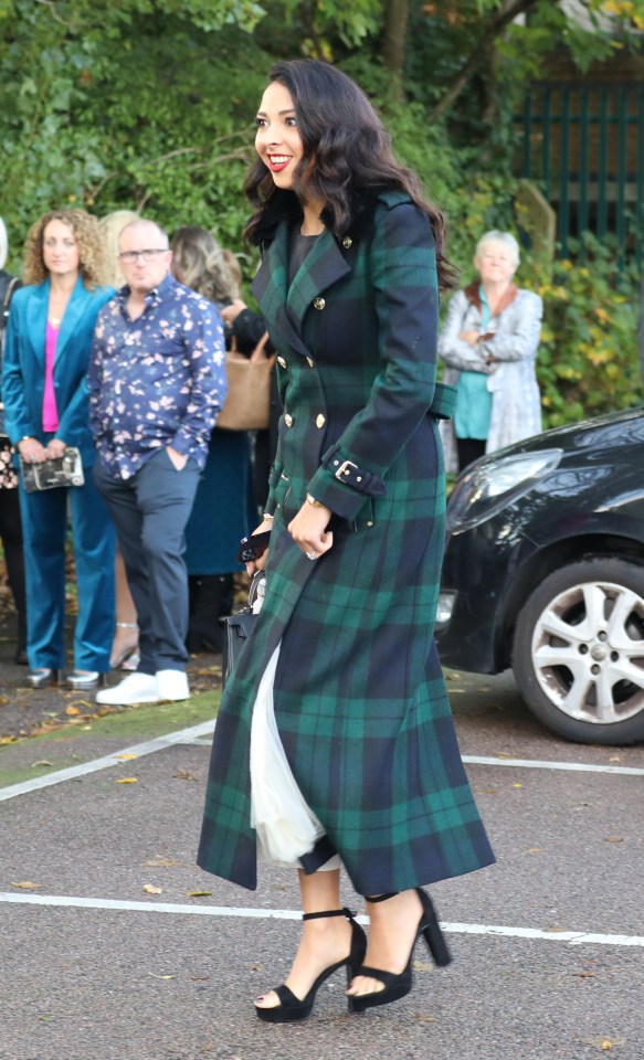 a woman in a plaid coat and black heels stands in a parking lot