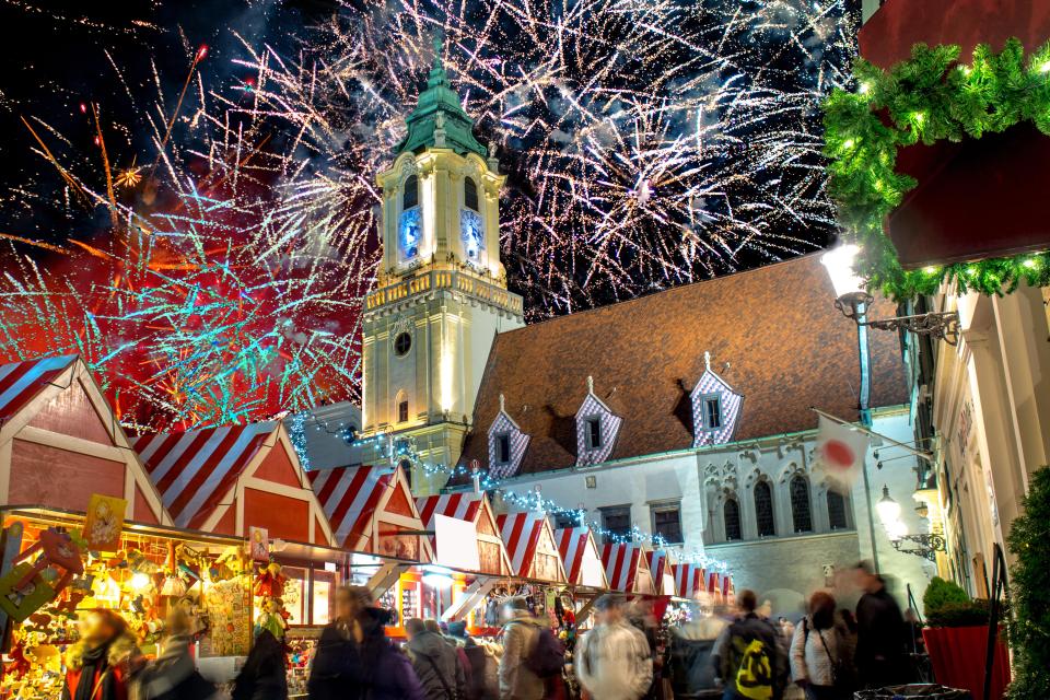 a crowd of people are gathered at a christmas market with fireworks in the background