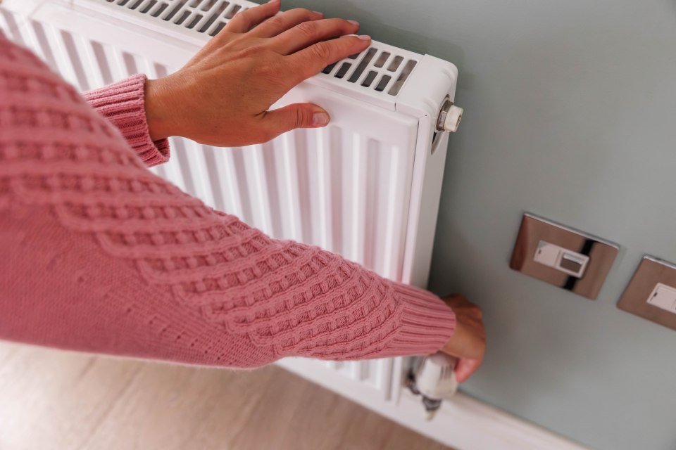 Top view of woman's hands in a wool pink jumper turning down the heating temperature on a home radiator using a thermostat. Energy crisis and cold weather concept