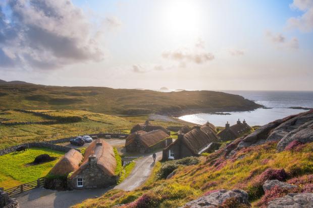 a row of thatched houses sit on a hill overlooking the ocean