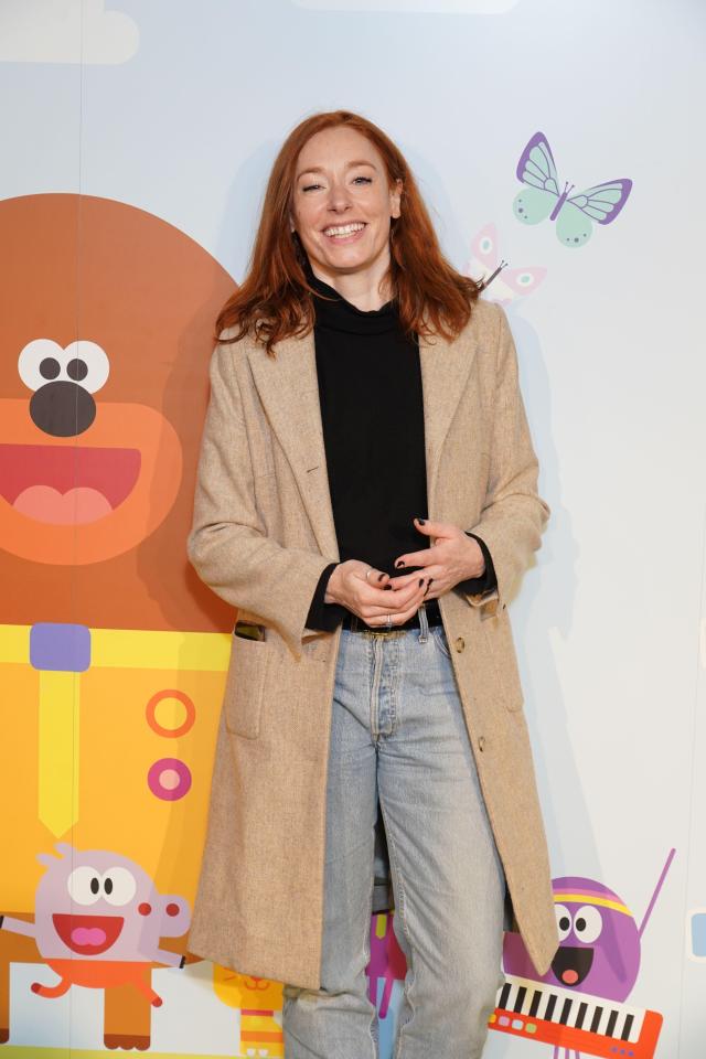 a woman in a tan coat stands in front of a cartoon character