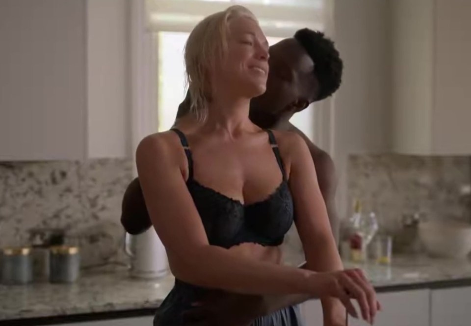 a man is kissing a woman in a bra in a kitchen .