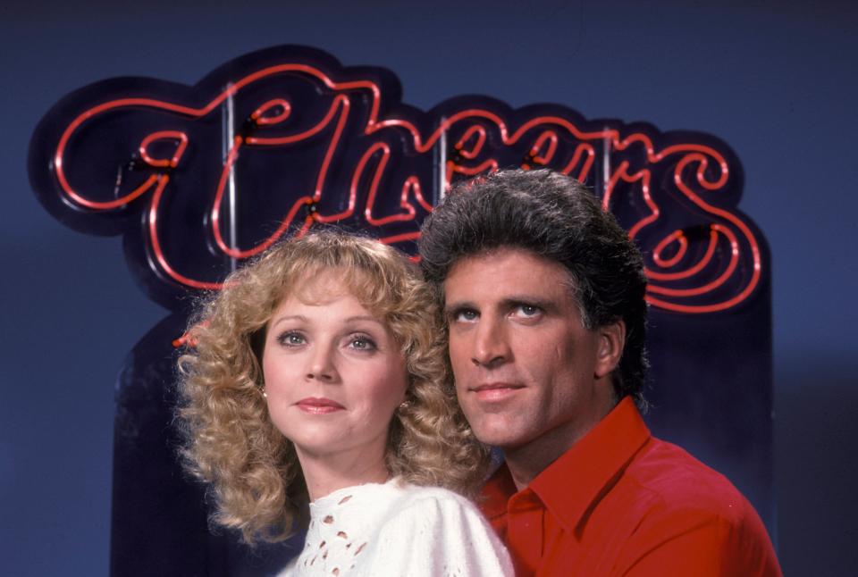 a man and a woman standing in front of a neon sign that says cheers