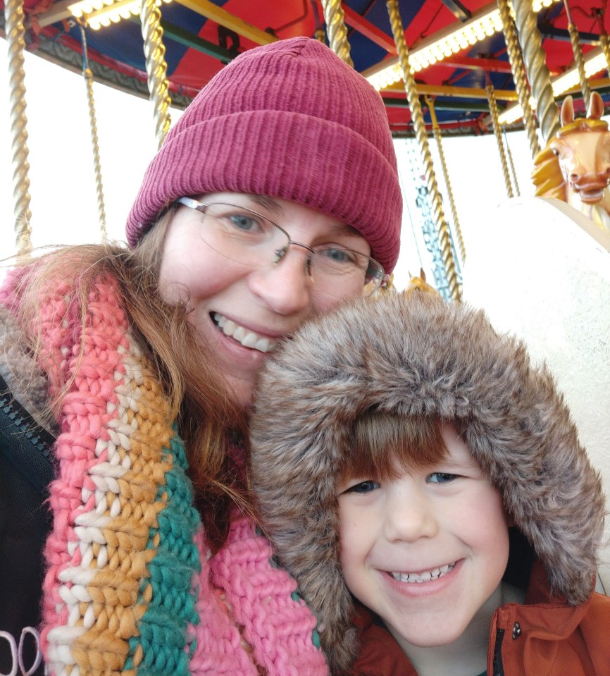 a woman and child are posing for a picture in front of a merry go round