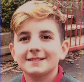 a young boy is smiling for the camera in front of a red fence .