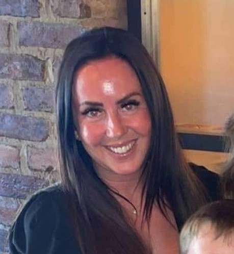 a woman is smiling in front of a brick wall while holding a child .