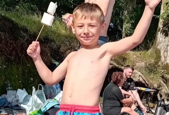 a shirtless boy is holding a marshmallow on a stick