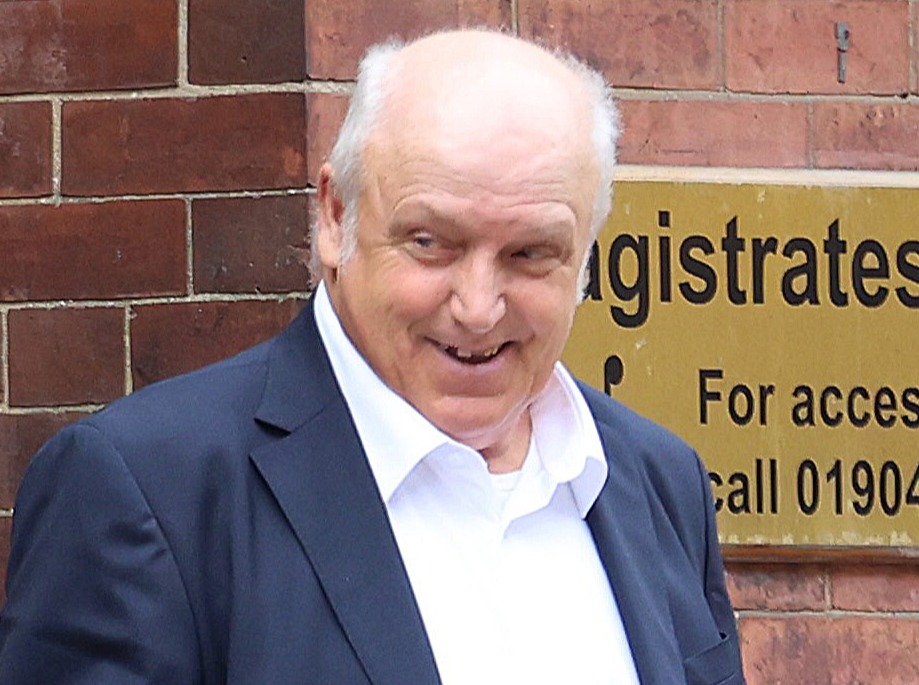 a man in a suit stands in front of a sign for the magistrates court