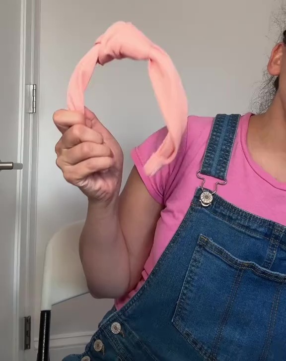 a woman in overalls is holding a pink headband