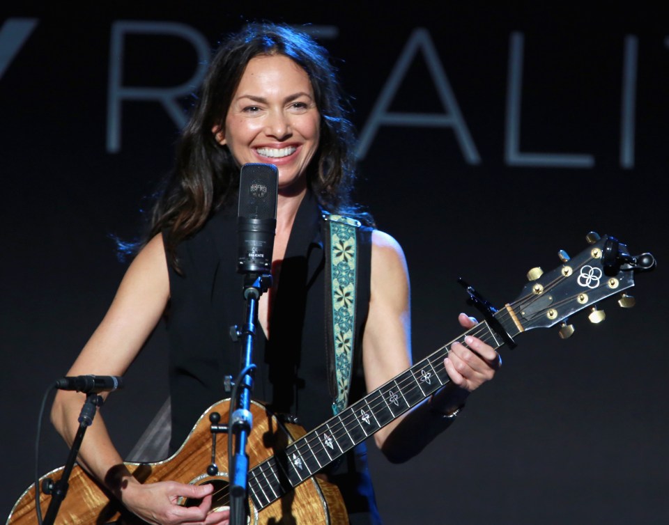 a woman playing a guitar in front of a sign that says realit