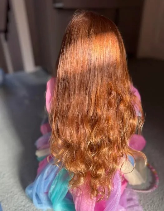 a little girl with long red hair is wearing a pink and blue dress