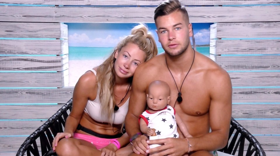 a man and woman holding a baby in front of a wooden wall