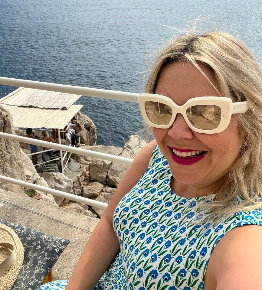 a woman wearing sunglasses is sitting on a balcony overlooking the ocean