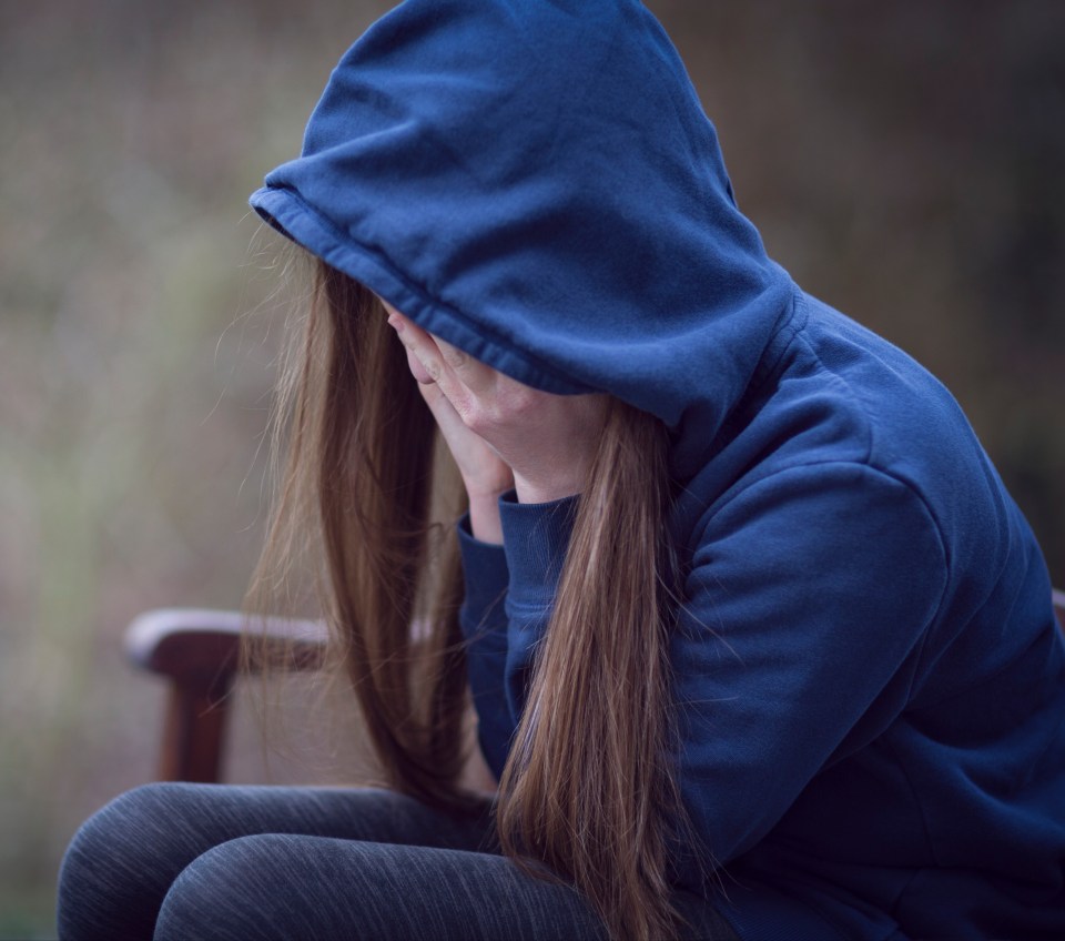 a girl in a blue hoodie covering her face with her hands