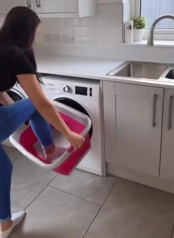 a woman is putting a pink bucket into a washing machine .