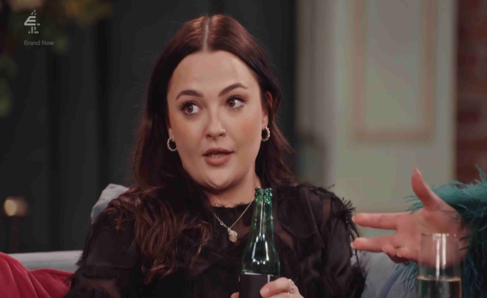 a woman sitting on a couch holding a bottle of beer and a glass