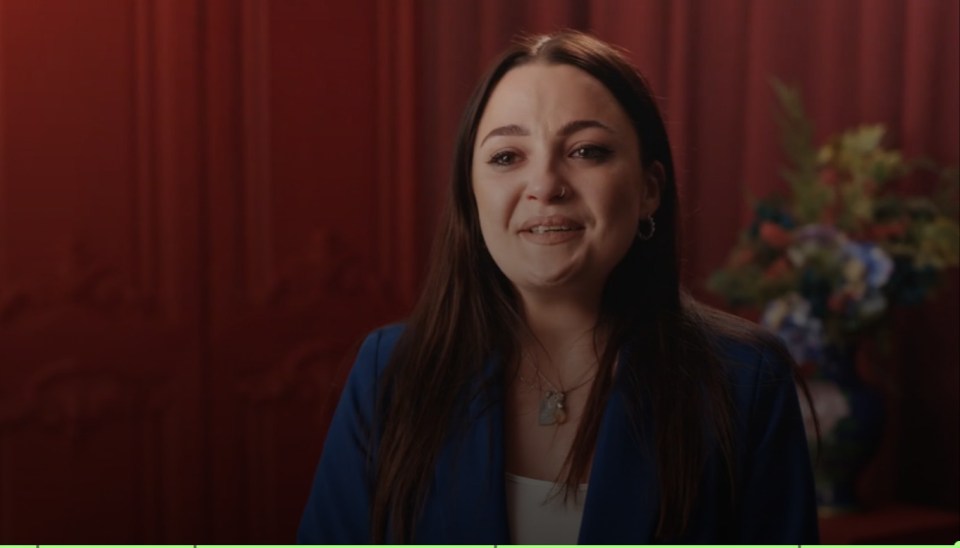 a woman in a blue jacket is smiling in front of a red curtain