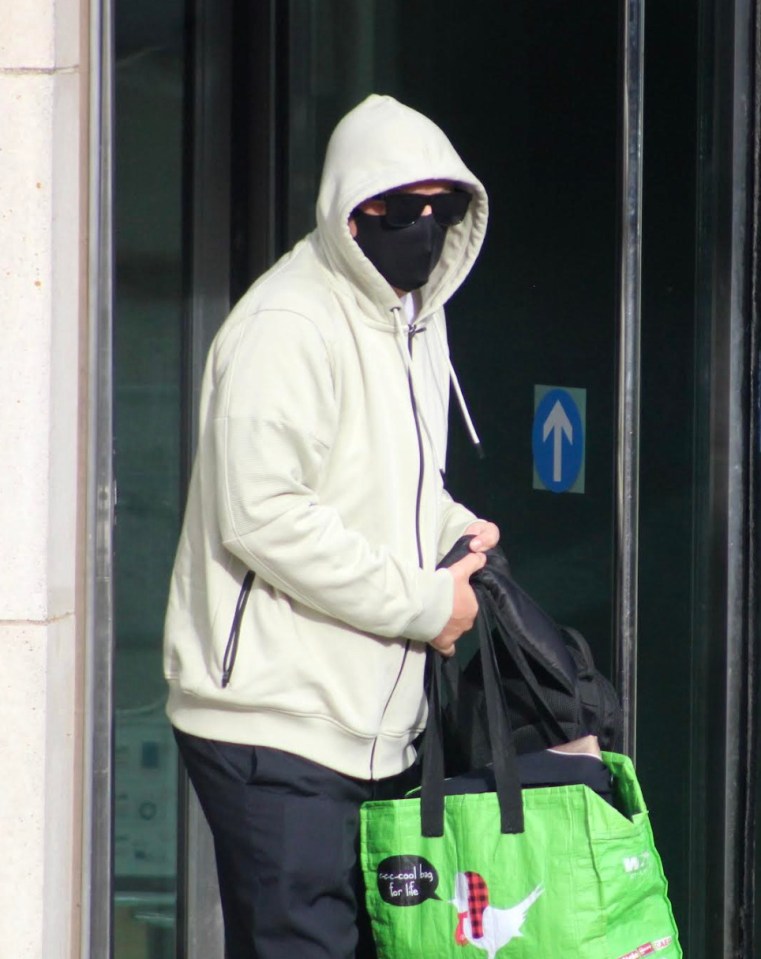 a man wearing a mask and a hoodie is carrying a green bag that says ' christmas ' on it