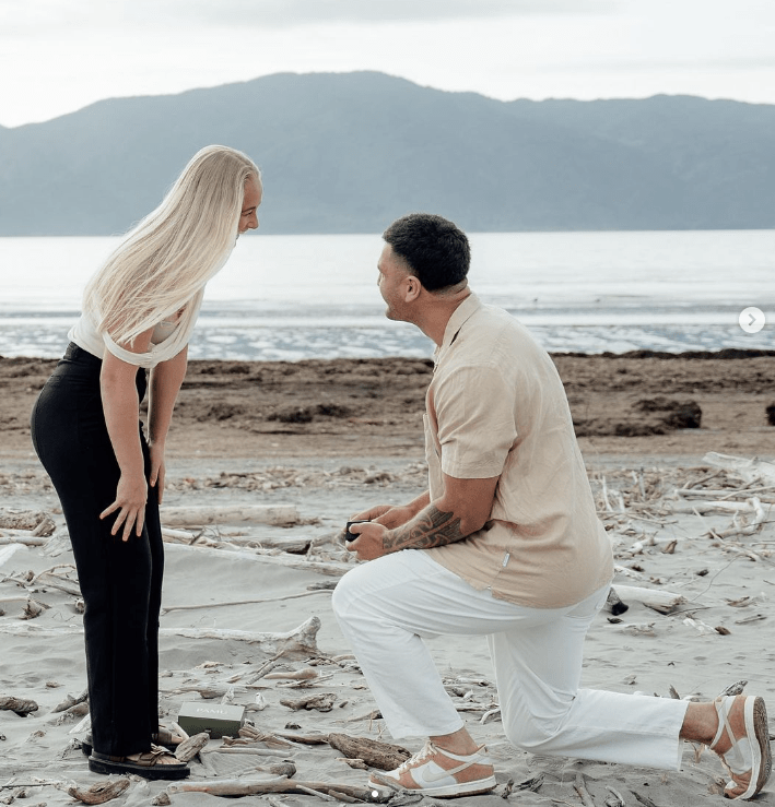 a man kneels down to propose to a woman on the beach