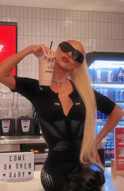 a woman holding a drink in front of a sign that says come on over baby