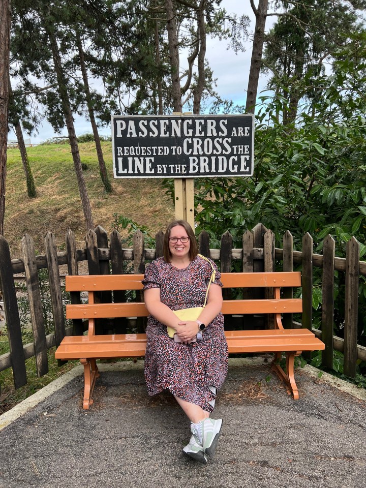 a woman sits on a bench under a sign that says passengers are requested to cross the line by the bridge