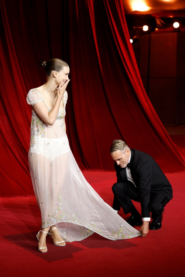 a man in a tuxedo adjusts a woman 's dress on a red carpet