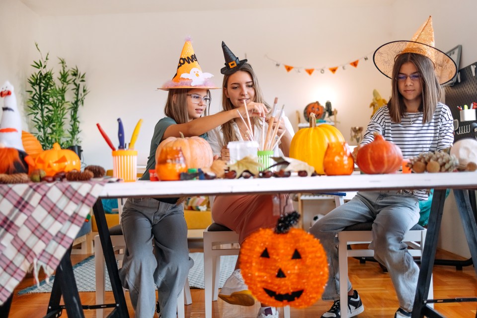 Family having fun at home with decorating for Halloween night. Painting together on pumpkins.