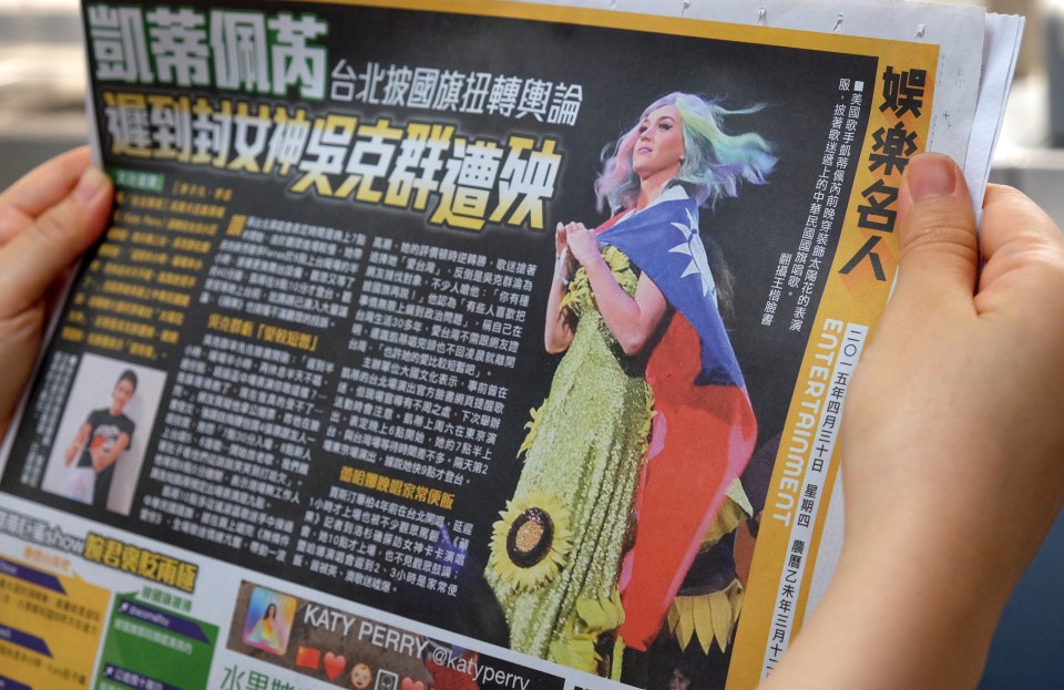 In this photo illustration taken on April 30, 2015, a local resident reads a newspaper showing US singer Katy Perry wearing Taiwan's national flag in Taipei. The intricacies of the "one China" policy may not have been uppermost on her mind, but US pop star Katy Perry caused a stir in Asia this week with her politically-charged choice of dress at a Taipei concert.  AFP PHOTO / Sam Yeh        (Photo credit should read SAM YEH/AFP via Getty Images)