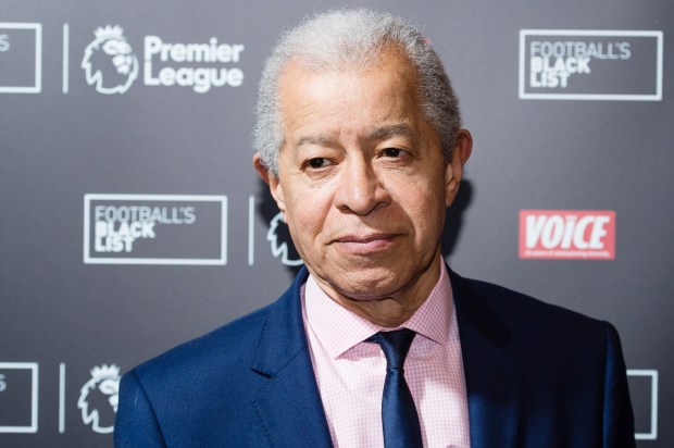 a man in a suit and tie stands in front of a premier league sign