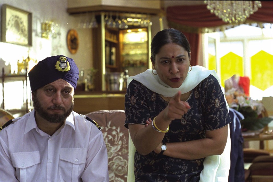 a man wearing a turban with a lion on it points at a woman