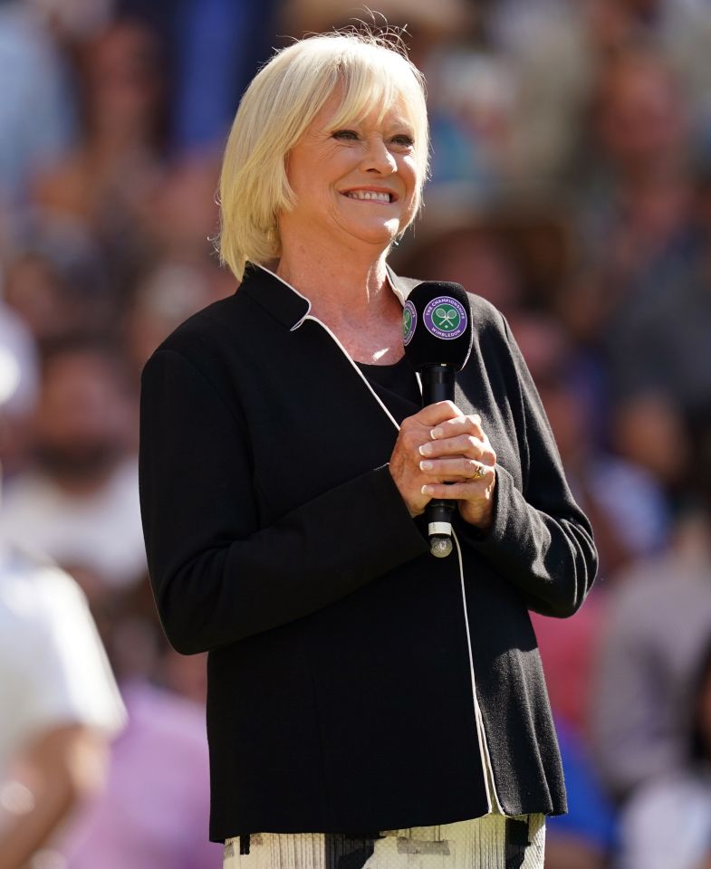 a woman wearing a wimbledon jacket holds a microphone