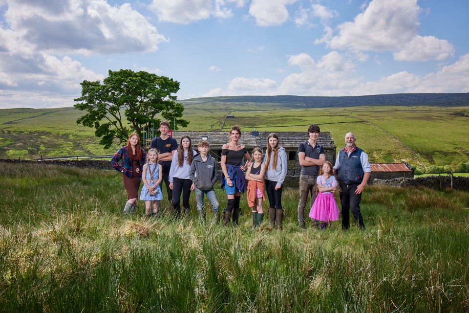 a group of people standing in a grassy field with one wearing a pink dress