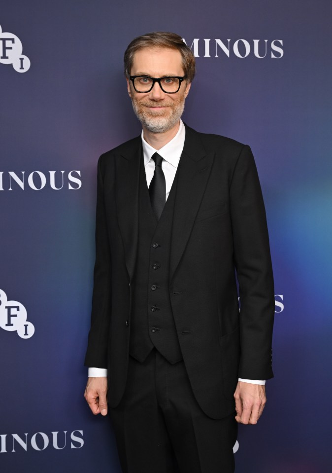 a man in a suit stands in front of a wall that says inous