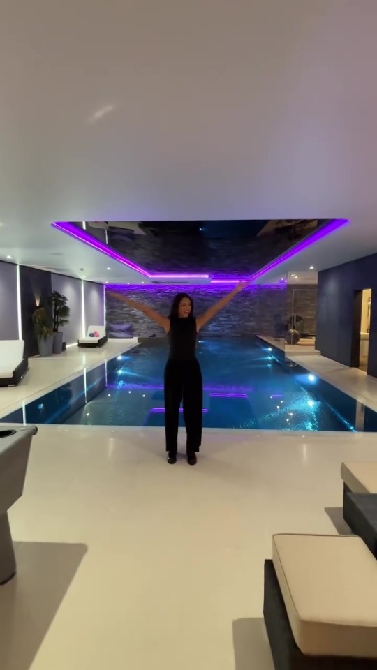 a woman stands in front of an indoor pool with her arms outstretched