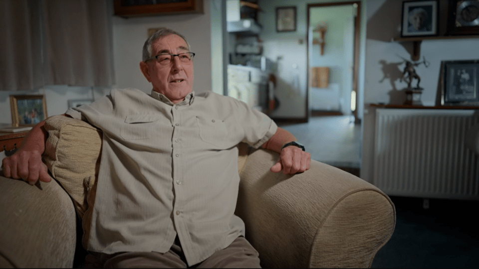 a man wearing glasses sits in a chair in a living room