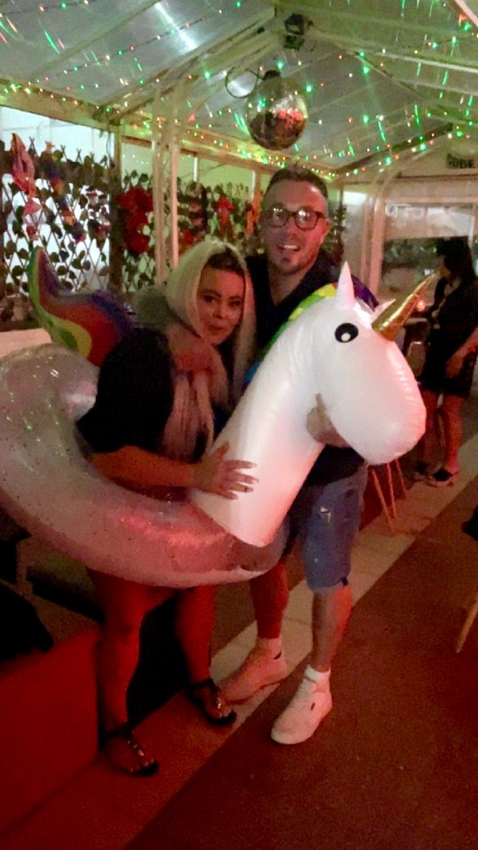 a man and a woman pose with an inflatable unicorn