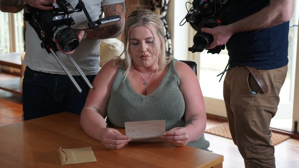 a woman sits at a table reading a letter from someone