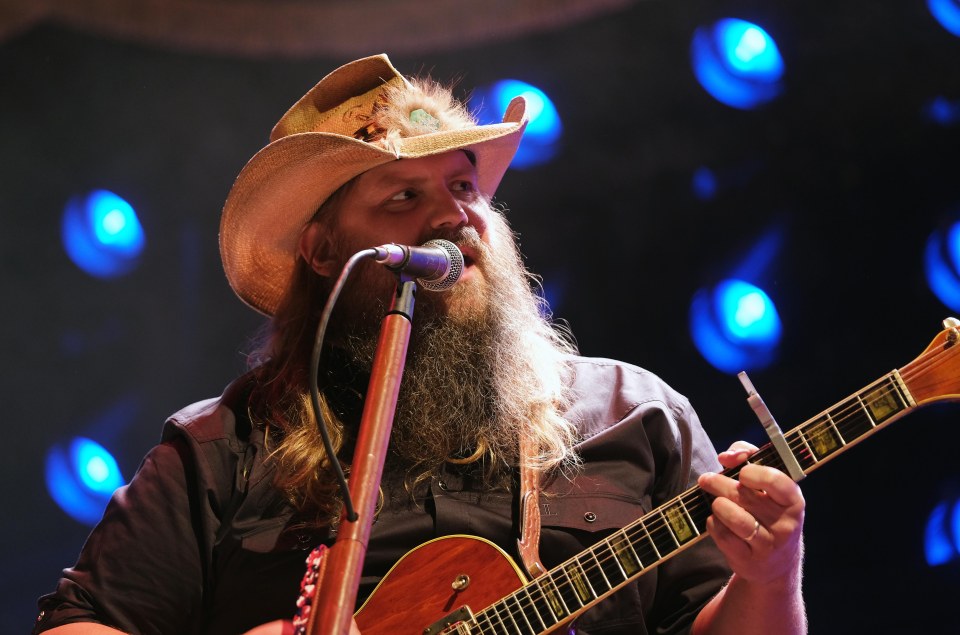 a man with a beard is singing into a microphone while holding a guitar