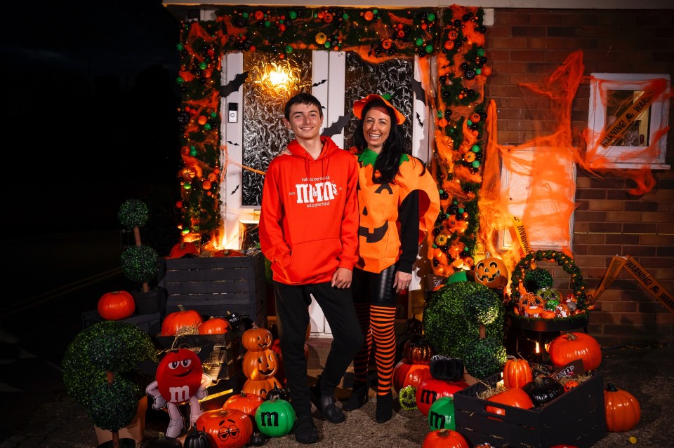 a boy and a woman pose in front of a house decorated for halloween